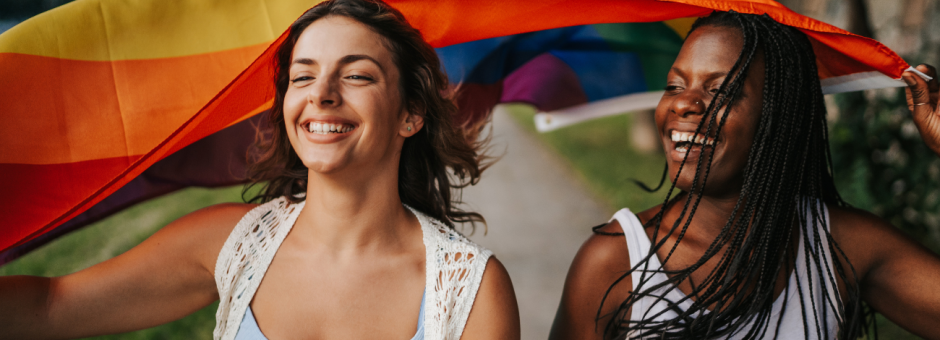 two young women hold a rainbow pride flag smiling